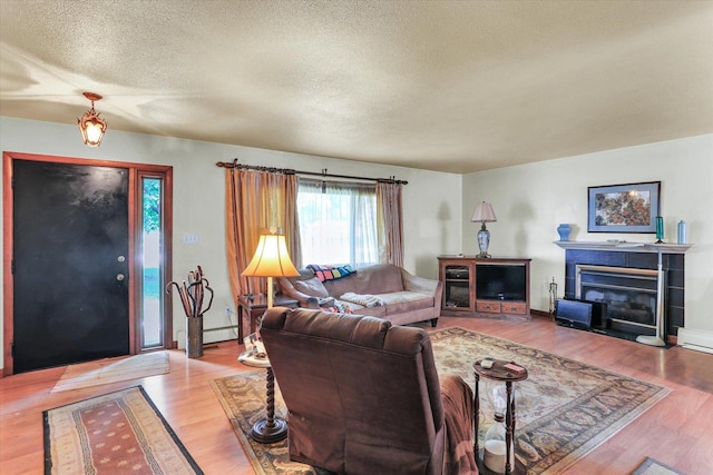 7 Birch Ln, Villa Grove, IL 61956 - living area with wood finished floors, a baseboard heating unit, a textured ceiling, and a tiled fireplace