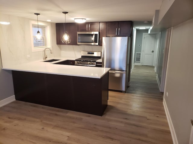 kitchen featuring appliances with stainless steel finishes, a sink, wood finished floors, a peninsula, and light countertops
