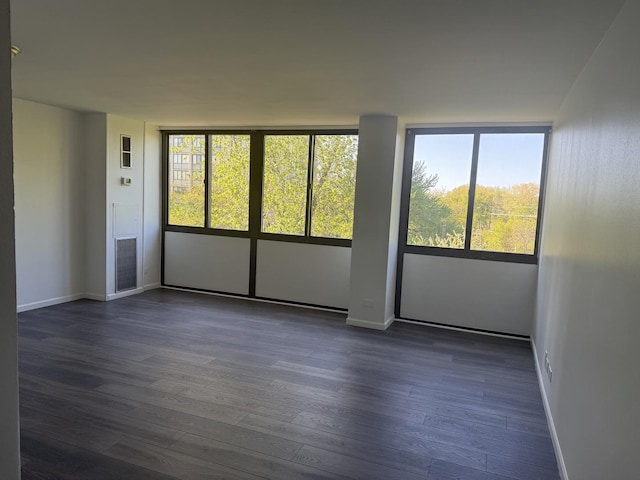 unfurnished room featuring healthy amount of natural light, dark wood finished floors, and baseboards