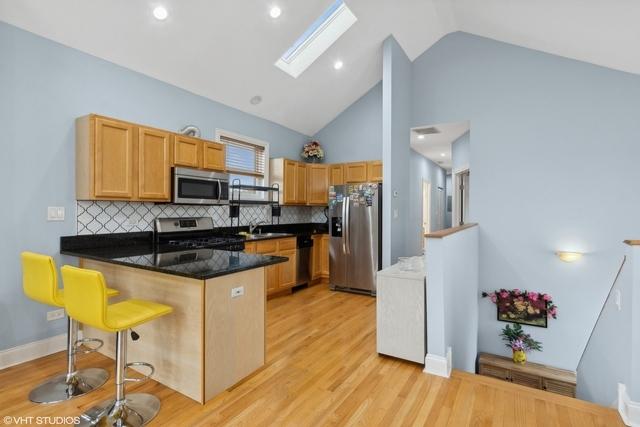 3934 W Argyle St Unit 3, Chicago, IL 60625 - kitchen featuring stainless steel appliances, a peninsula, a sink, a skylight, and tasteful backsplash