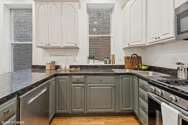 kitchen featuring stainless steel appliances, white cabinets, dark stone countertops, a sink, and gray cabinetry