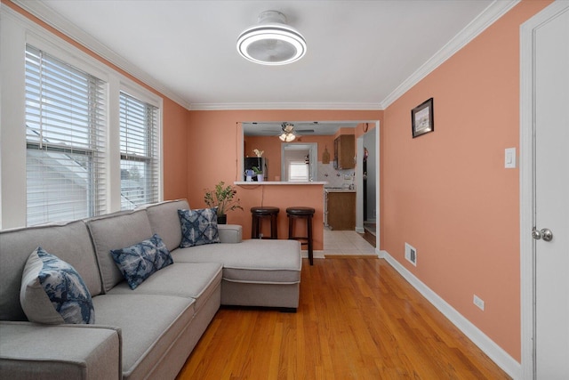 living area featuring healthy amount of natural light, ornamental molding, light wood-style floors, baseboards, and ceiling fan