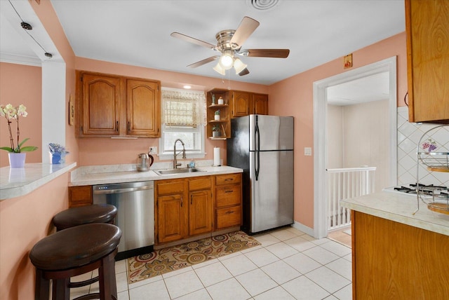 kitchen featuring appliances with stainless steel finishes, a sink, brown cabinets, a ceiling fan, and light countertops