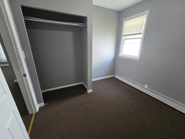 unfurnished bedroom with baseboard heating, dark colored carpet, baseboards, and a closet