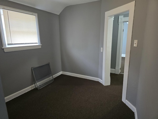 spare room featuring dark carpet, vaulted ceiling, and baseboards