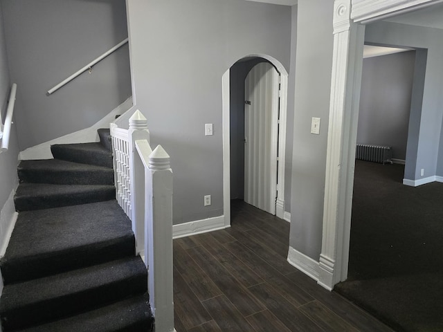 staircase featuring radiator, wood finished floors, baseboards, and arched walkways