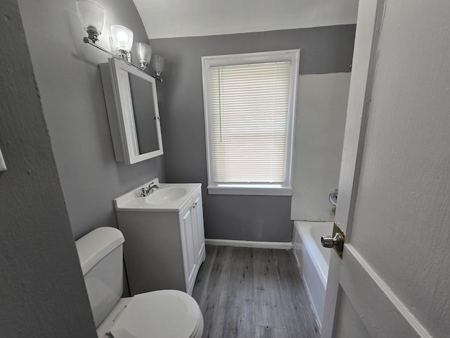 full bath with wood finished floors, toilet, vanity, a bathtub, and baseboards