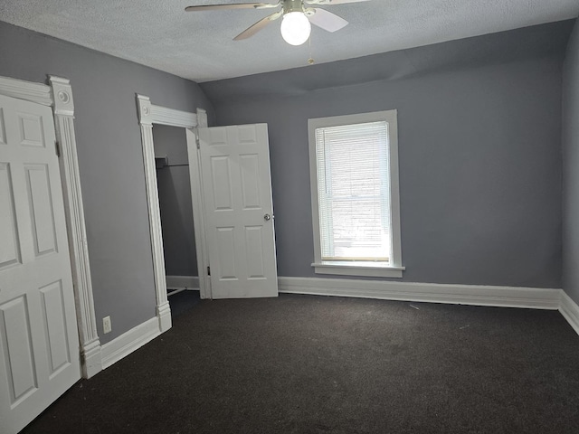 unfurnished bedroom with dark carpet, a textured ceiling, baseboards, and ceiling fan