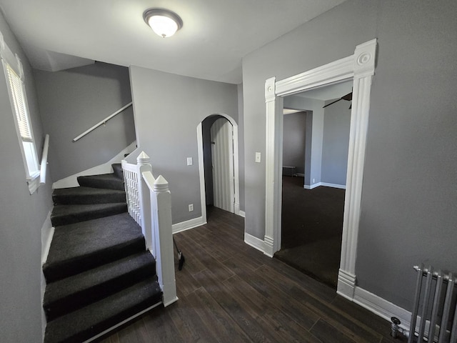 staircase with arched walkways, radiator, wood finished floors, and baseboards