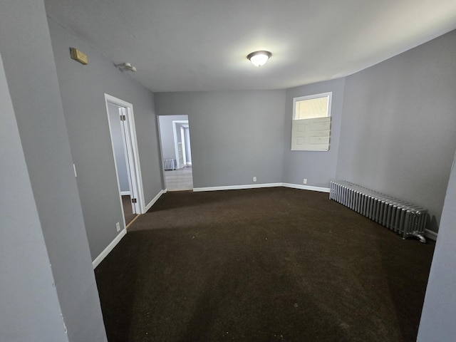 spare room featuring radiator heating unit, baseboards, and dark colored carpet
