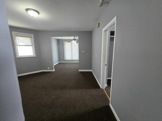 hallway with baseboards and dark colored carpet