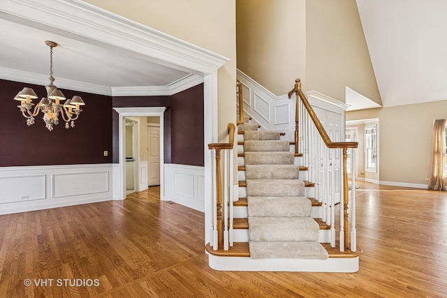 9310 Nicklaus Ln, Lakewood, IL 60014 - stairs featuring wood finished floors, a chandelier, a towering ceiling, a wainscoted wall, and ornamental molding