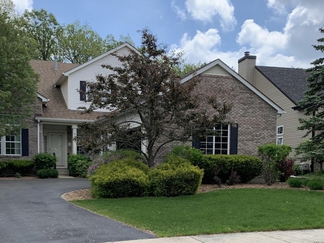 view of front of house featuring a front lawn, brick siding, a shingled roof, and a chimney