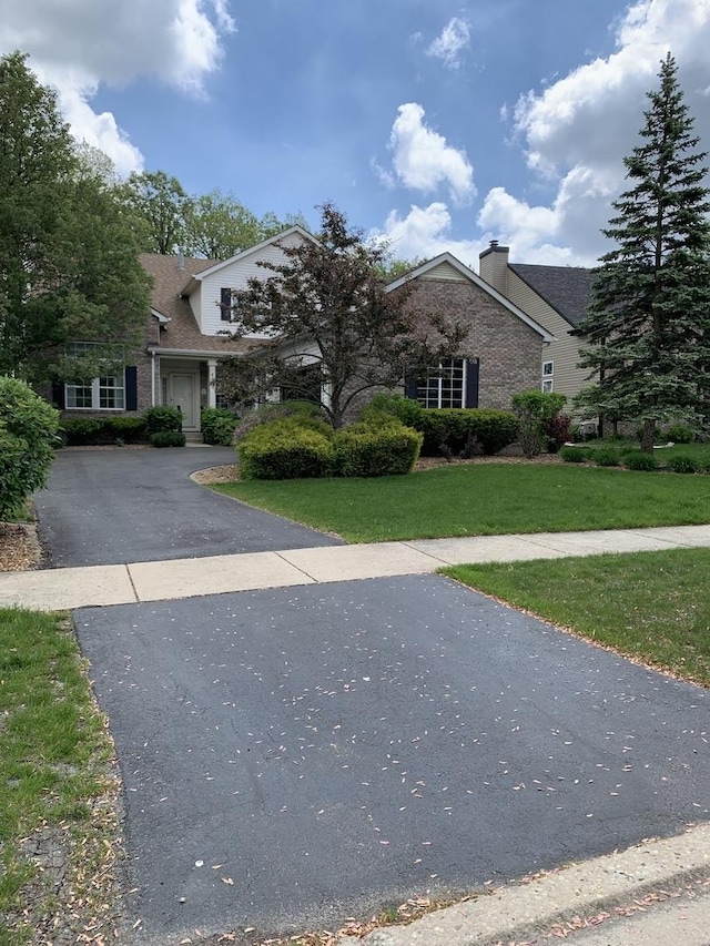view of front facade featuring a chimney, brick siding, a front lawn, asphalt driveway, and roof with shingles