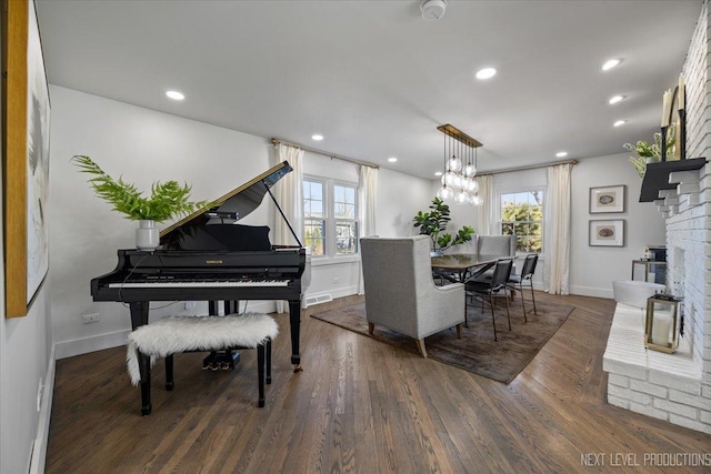 dining space featuring baseboards, wood finished floors, recessed lighting, a chandelier, and a brick fireplace