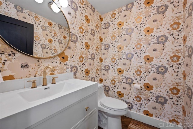 bathroom with wallpapered walls, toilet, vanity, and baseboards