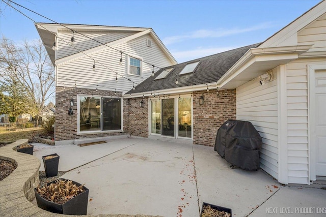 rear view of property featuring brick siding, a patio, and roof with shingles