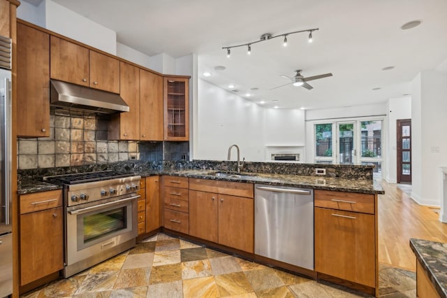 kitchen with appliances with stainless steel finishes, under cabinet range hood, a sink, a peninsula, and backsplash