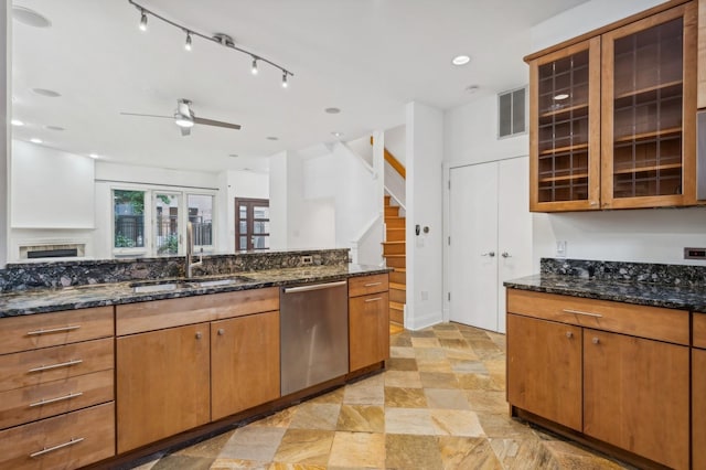 kitchen featuring dishwasher, a sink, ceiling fan, dark stone counters, and glass insert cabinets