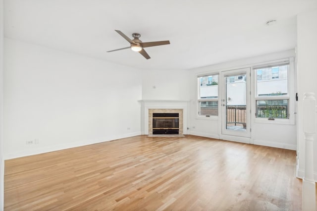 unfurnished living room featuring ceiling fan, light wood finished floors, a tiled fireplace, and baseboards