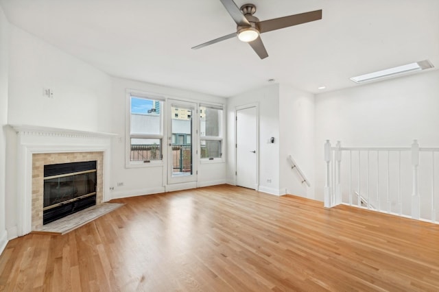 unfurnished living room with wood finished floors, ceiling fan, a fireplace, and baseboards