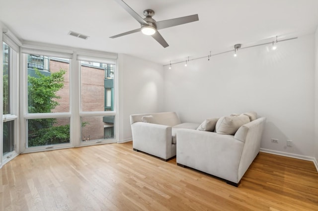 living area featuring track lighting, light wood-style flooring, a ceiling fan, and baseboards