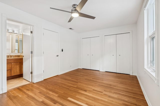 unfurnished bedroom featuring multiple closets, light wood-style floors, ensuite bathroom, and baseboards