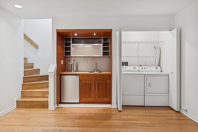 washroom with washing machine and clothes dryer, bar with sink, light wood finished floors, and baseboards