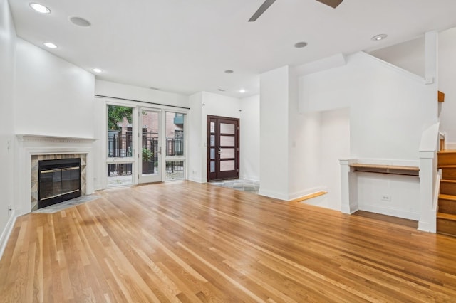 unfurnished living room with wood finished floors, a tiled fireplace, ceiling fan, stairway, and baseboards