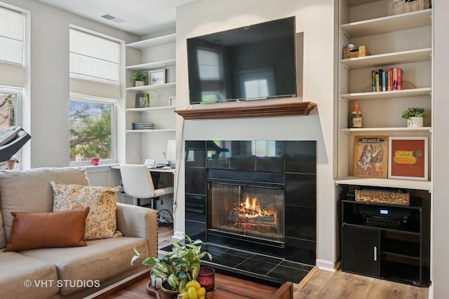 living area featuring wood finished floors, a tile fireplace, and built in features