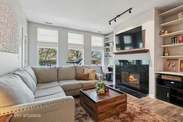 living area featuring wood finished floors, healthy amount of natural light, a fireplace, and built in shelves