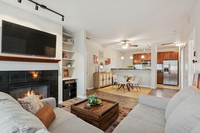 living area featuring rail lighting, light wood finished floors, a ceiling fan, and baseboards