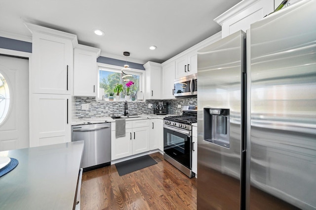 kitchen with appliances with stainless steel finishes, a sink, backsplash, white cabinets, and dark wood finished floors