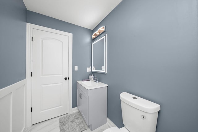 half bathroom featuring vanity, toilet, and marble look tiles
