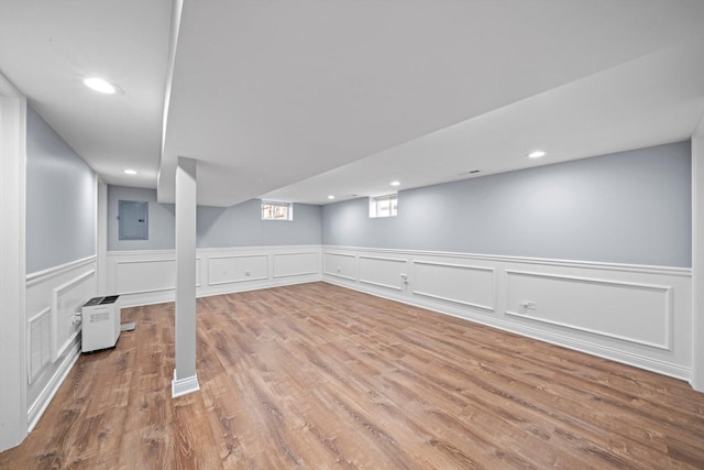 basement featuring electric panel, wood finished floors, a wainscoted wall, a decorative wall, and recessed lighting