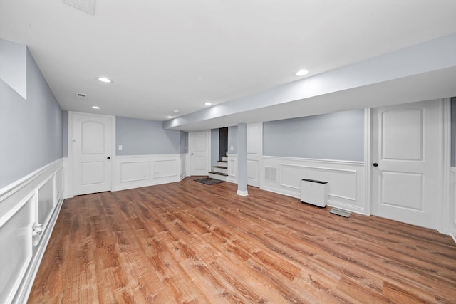 finished below grade area featuring stairs, light wood finished floors, wainscoting, a decorative wall, and recessed lighting