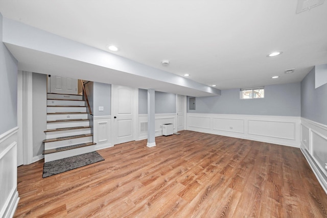 basement with wood finished floors, electric panel, a wainscoted wall, stairs, and a decorative wall