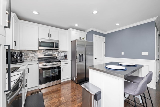 kitchen with appliances with stainless steel finishes, ornamental molding, a wainscoted wall, dark wood-style floors, and white cabinets