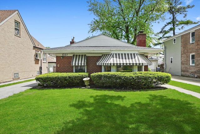 view of front of home featuring a chimney, a front lawn, brick siding, and roof with shingles
