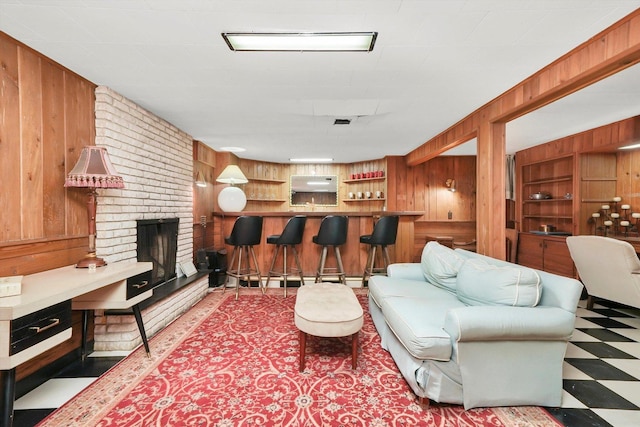 living room with wooden walls, tile patterned floors, a dry bar, and a fireplace