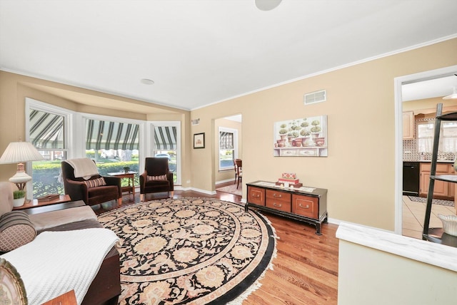living area with crown molding, light wood-style floors, and baseboards