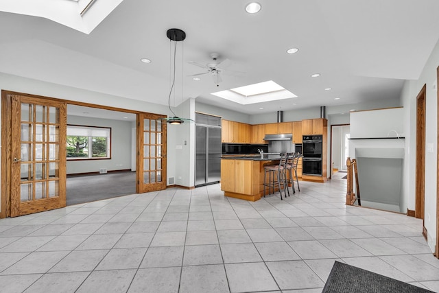 6801 N Lexington Ln, Niles, IL 60714 - kitchen featuring a skylight, dark countertops, a breakfast bar, under cabinet range hood, and recessed lighting