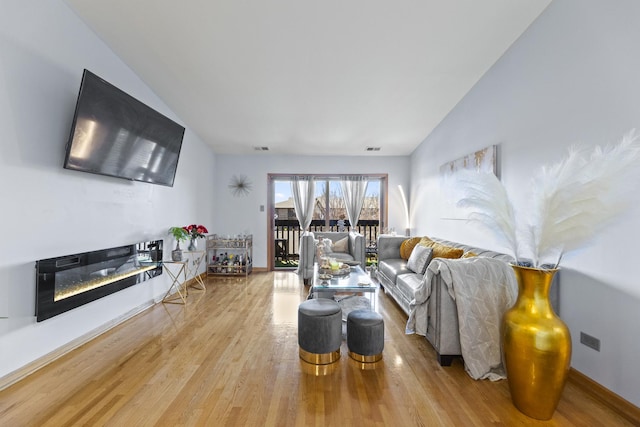 living room featuring wood finished floors, vaulted ceiling, and a glass covered fireplace