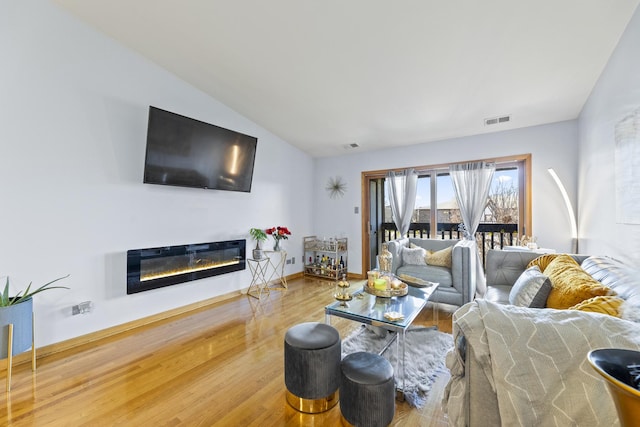 living room featuring wood finished floors, a glass covered fireplace, and vaulted ceiling