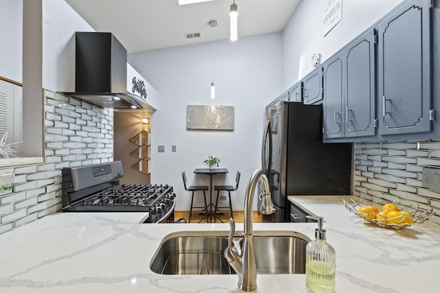 kitchen with stainless steel gas range, wall chimney range hood, a sink, freestanding refrigerator, and decorative backsplash