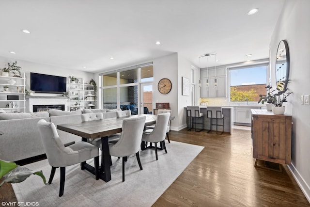 dining space with wood finished floors, a glass covered fireplace, recessed lighting, and baseboards