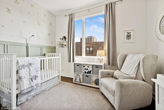 bedroom with wainscoting, a nursery area, and a decorative wall