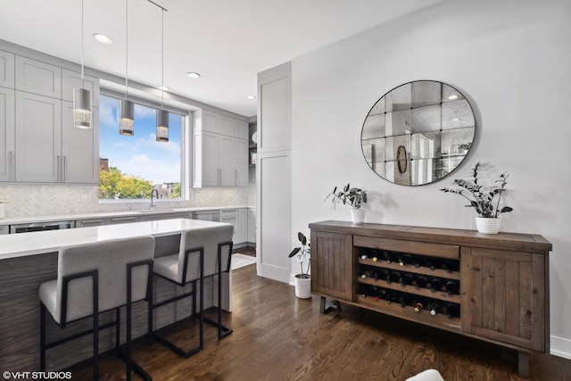 kitchen with a breakfast bar, light countertops, tasteful backsplash, a sink, and dark wood-type flooring