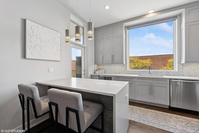 kitchen with stainless steel dishwasher, a sink, gray cabinetry, a kitchen bar, and backsplash