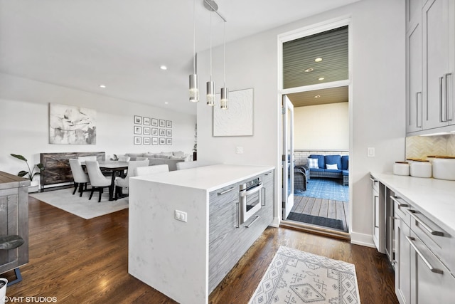 kitchen with a peninsula, dark wood-style floors, light countertops, pendant lighting, and open floor plan